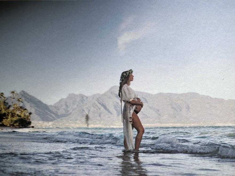 Sara, founder of Spa Mama Maui, pregnant and standing in the ocean with the West Maui Mountains behind her